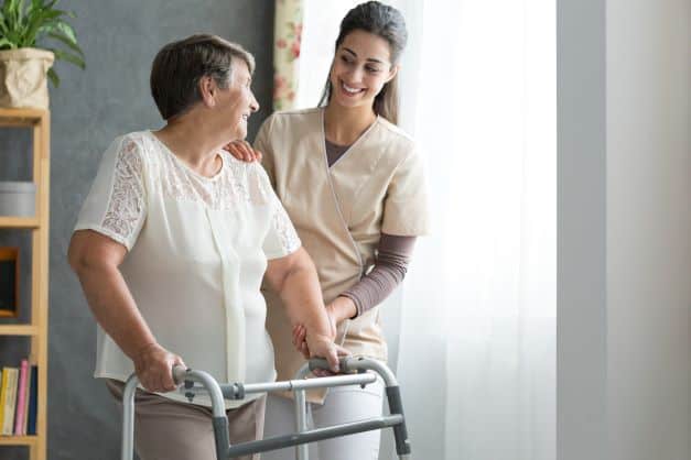 Elderly woman with walker being supported by caregiver
