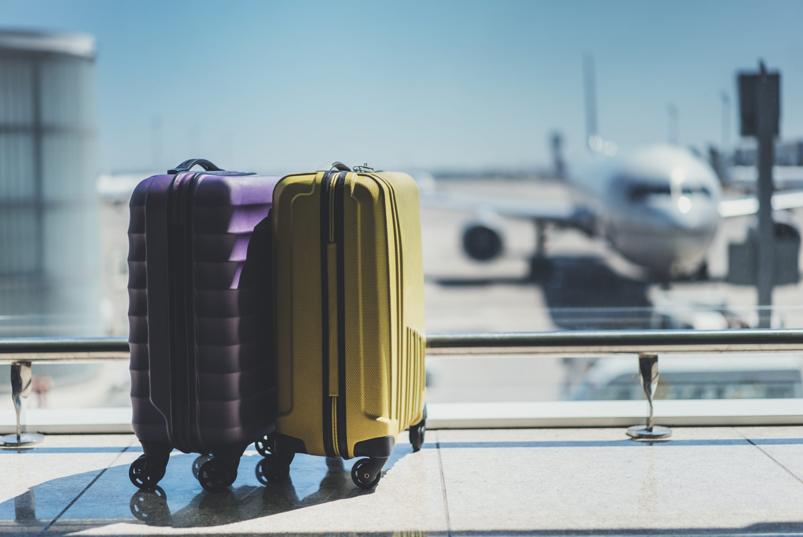 A purple suitcase and a yellow suitcase next to each other at an aiport.