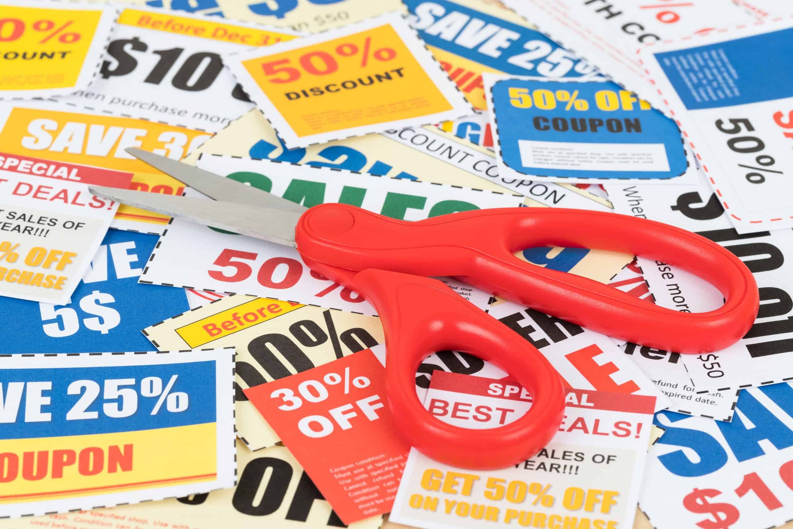Pair of scissors with red handles on top of pile of coupons