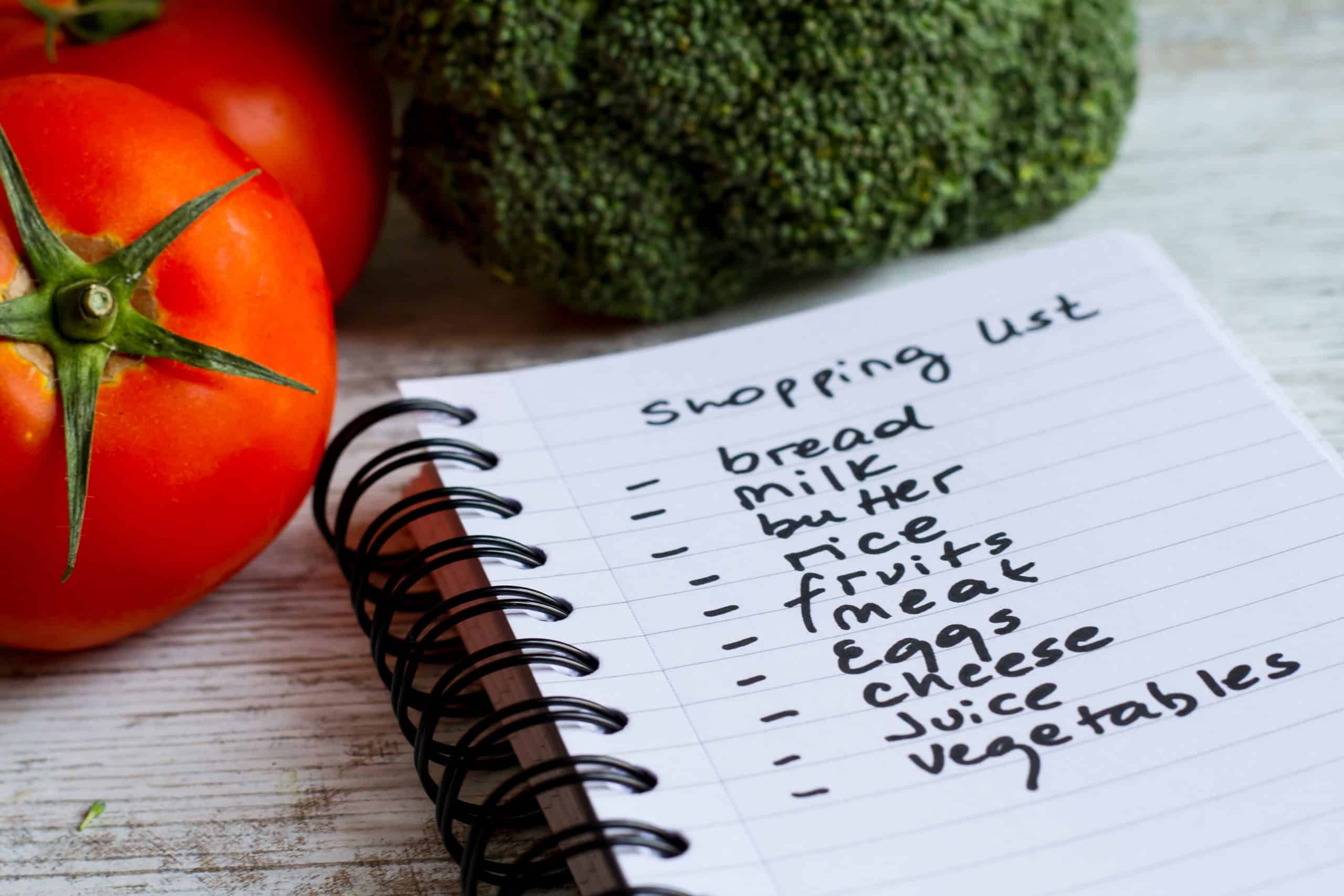 Red tomatoes and green broccoli next to shopping list written in a small notebook