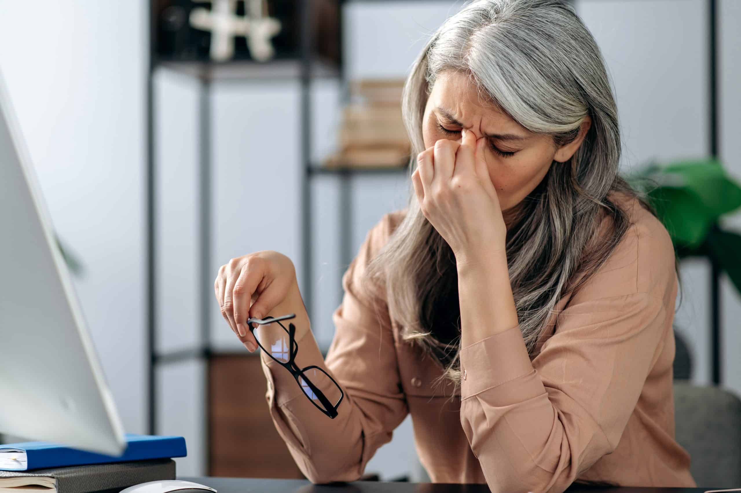 Woman with gray hair holding her head during a migraine