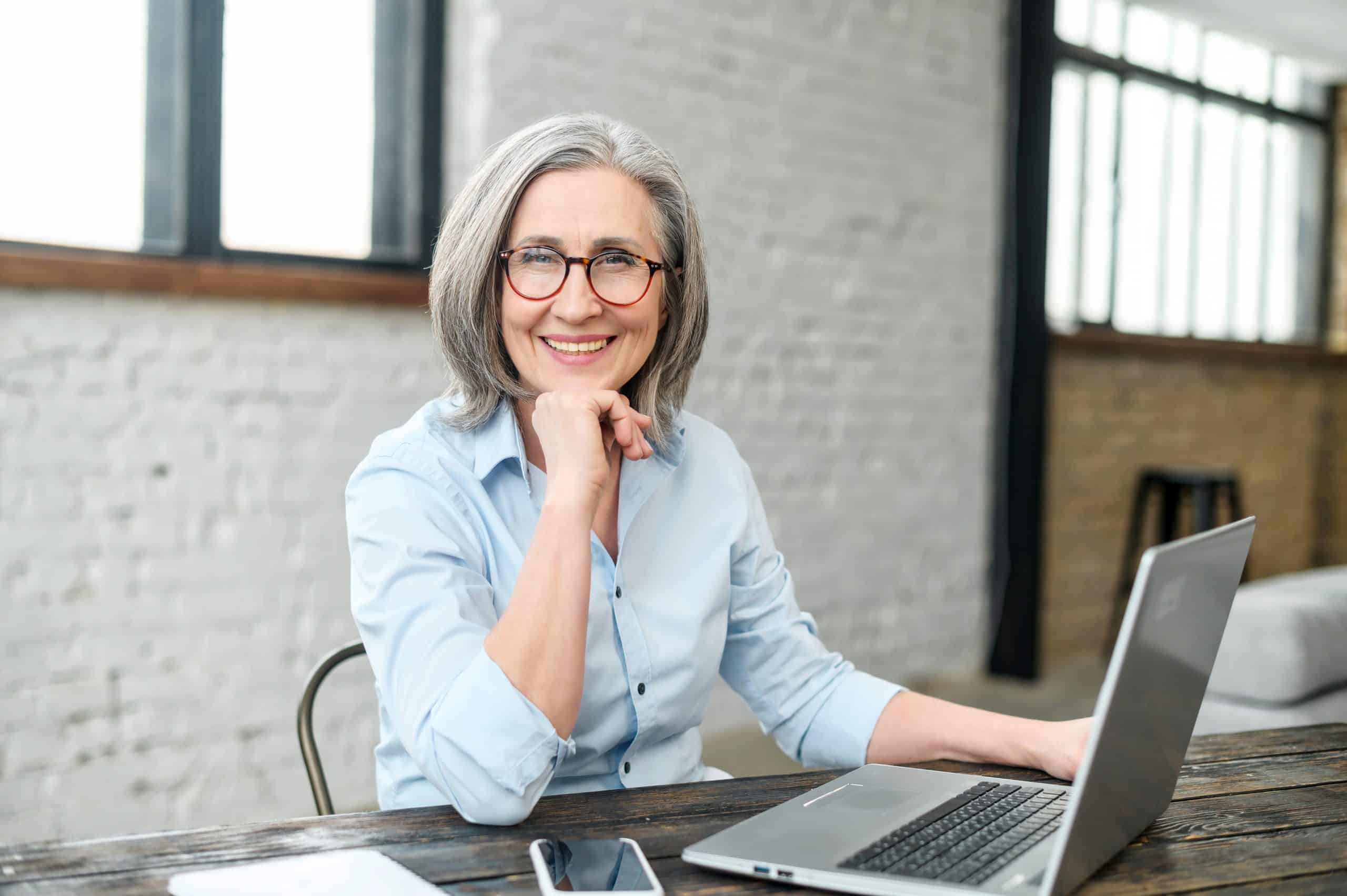 Woman with gray hair and glasses working on a laptop